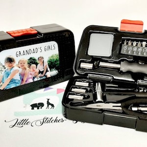 May include: A black tool kit with a personalised photo label that says "Grandad's Girls". The kit includes a screwdriver, pliers, and various bits.