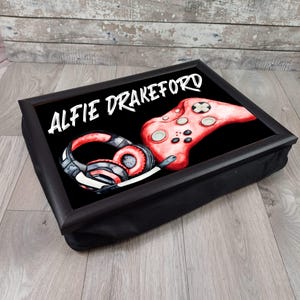 May include: A black tray with a red and black gaming controller and headphones. The tray has a black cushion and the text "Alfie Drakeford" is printed on the tray.