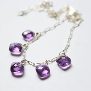May include: A silver chain necklace with five dangling amethyst gemstones. The gemstones are faceted and have a light purple hue.