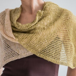 May include: A light brown and green knitted shawl with a lacy pattern. The shawl is draped around a person's shoulders.
