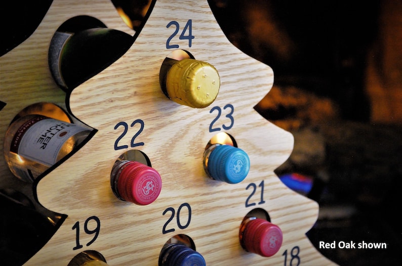 May include: A wooden Christmas tree wine bottle holder with 24 numbered slots. The tree is made of red oak wood and has a natural finish. The slots are filled with wine bottles with colourful bottle caps.
