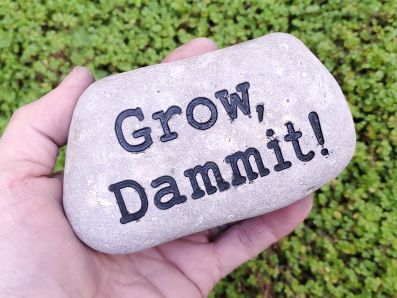 Puede incluir: Una piedra gris con las palabras "Grow, Dammit!" pintadas en negro.