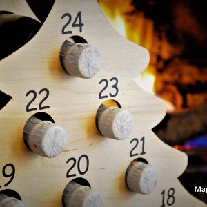 May include: Wooden Christmas tree wine rack with 24 numbered slots for wine bottles. The rack is made of light wood and has a natural finish. The numbers are black and are printed on the front of the rack. The rack is shown in front of a fireplace.