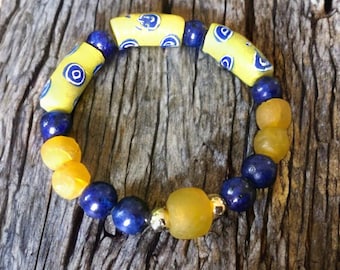 May include: A yellow and blue beaded bracelet with a gold accent. The bracelet is made of round and cylindrical beads.