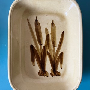 May include: A rectangular ceramic baking dish with a cream-coloured glaze and a brown painted design of three stylised cattails.