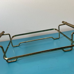 May include: A gold-toned metal serving tray with two handles. The tray is rectangular and has a simple, modern design.