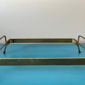 May include: A gold metal tray with a textured surface and two handles. The tray has a rectangular shape and is sitting on a blue surface.