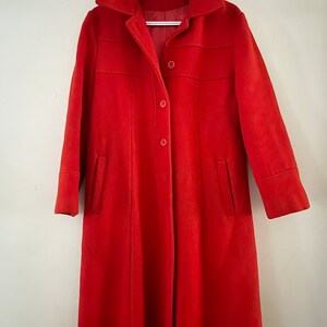 May include: A long red coat with a collar and button closure. The coat has two pockets and long sleeves.