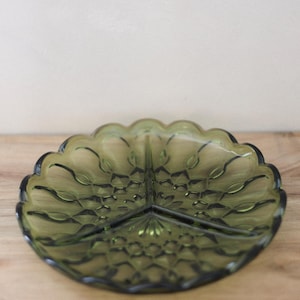 Peut inclure: Un plat de service divisé vert olive vintage avec un bord festonné. Le plat en verre comporte trois compartiments et un motif texturé. Il est présenté sur une surface en bois.