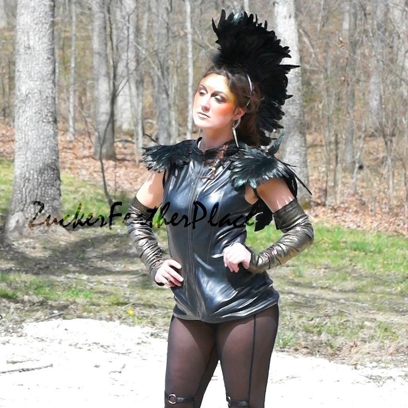 Puede incluir: Una mujer lleva un chaleco de cuero negro con hombreras de plumas negras y un tocado de plumas negras. Lleva leggings negros y guantes negros. El texto "Zucker Feather Place" es visible en la imagen.
