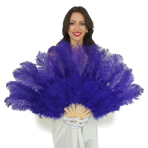 May include: A purple ostrich feather fan with a wooden handle. The fan is held by a person wearing a white dress.