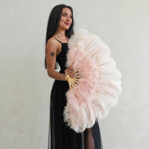 Puede incluir: Una mujer con un vestido negro sostiene un gran abanico de plumas rosa y blanco. El abanico est&aacute; cerrado y tiene un mango de madera.
