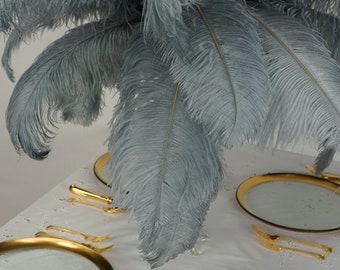 May include: A table setting with two gold-rimmed plates and cutlery. A large plume of grey ostrich feathers hangs over the table.
