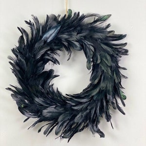 Peut inclure: Une couronne circulaire compos&eacute;e de nombreuses plumes noires superpos&eacute;es. Les plumes sont dispos&eacute;es selon un motif dense et chevauchant, cr&eacute;ant un aspect textur&eacute; et volumineux avec de subtils reflets verts et bleus visibles sur certaines pointes.