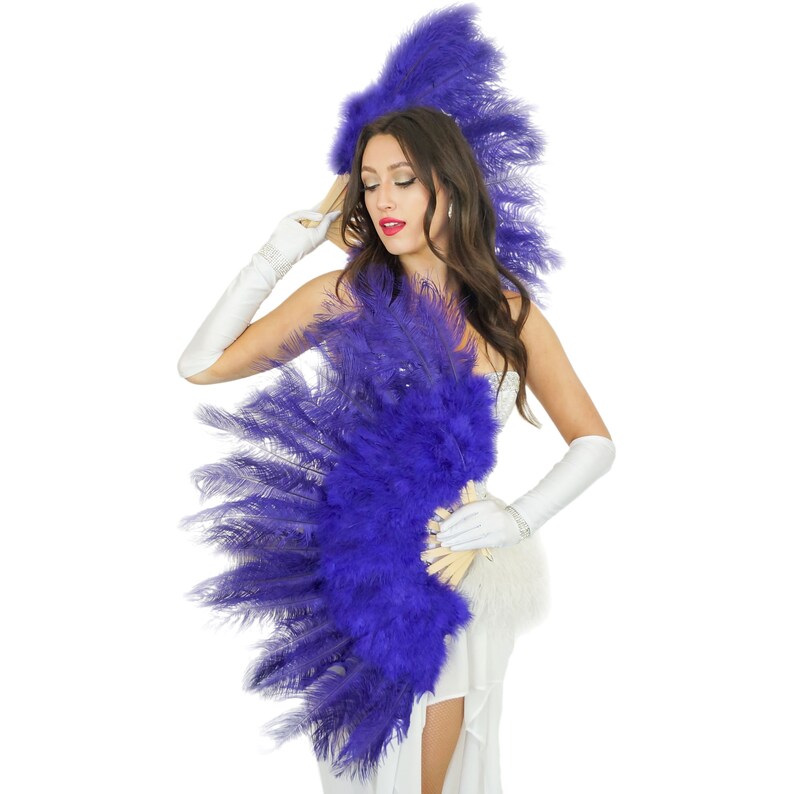 May include: A woman wearing a white dress and long white gloves holds a large purple feather fan. She is wearing a purple feather headdress.