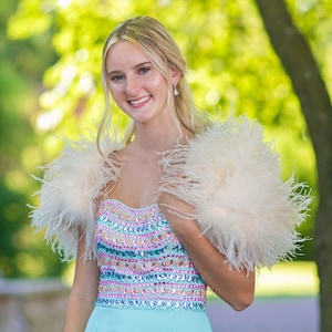 May include: A young woman wearing a light blue dress with a beaded bodice and a white feather boa. She is smiling and looking at the camera.