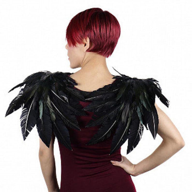 Puede incluir: Alas de hombro de plumas negras con un brillo verde iridiscente. Las alas est&aacute;n hechas de plumas naturales y est&aacute;n unidas a una banda el&aacute;stica negra.