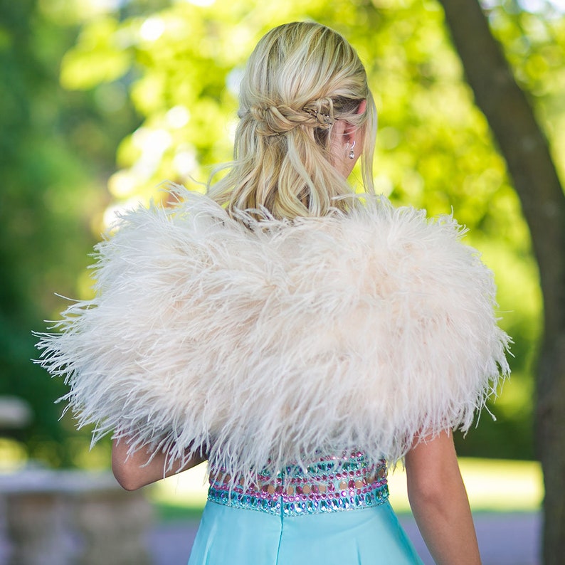 May include: A white feather boa with a light blue dress underneath. The boa is worn around the shoulders and is made of soft, fluffy feathers.