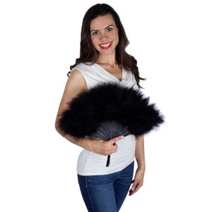 May include: A handheld folding fan featuring dense black feathers attached to a black frame. The fan is fully extended in a semi-circular shape, showcasing the soft, fluffy texture of the dark plumage and the structured, articulated ribs of the handle.
