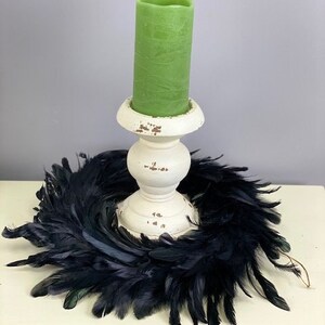 Peut inclure: Une bougie pilier cylindrique vert clair est plac&eacute;e dans un bougeoir en bois blanc &agrave; l'aspect vieilli. La base du bougeoir est entour&eacute;e d'une couronne circulaire faite de plumes noires fonc&eacute;es, cr&eacute;ant un ensemble d&eacute;coratif contrast&eacute;.
