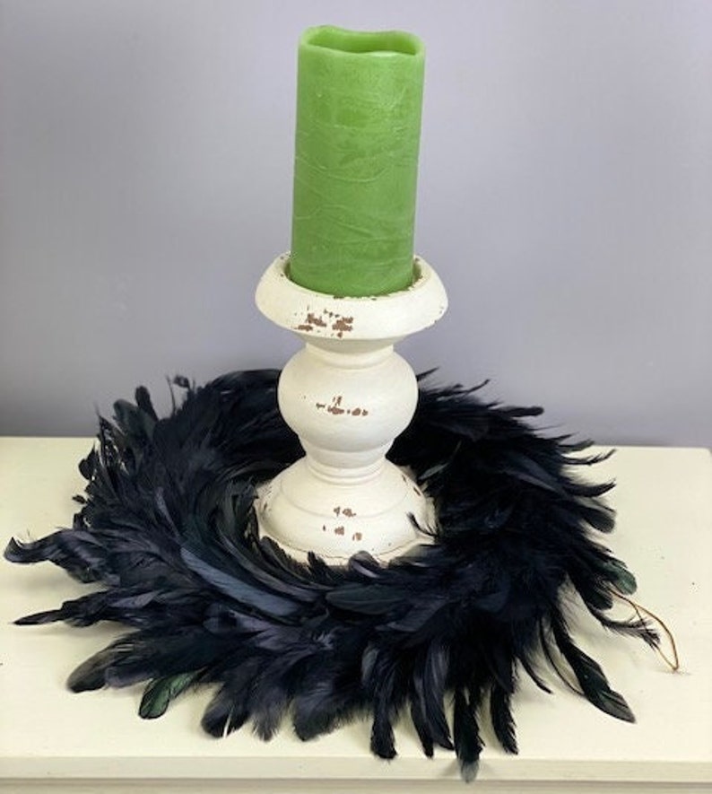 Peut inclure: Une bougie pilier cylindrique vert clair est plac&eacute;e dans un bougeoir en bois blanc &agrave; l'aspect vieilli. La base du bougeoir est entour&eacute;e d'une couronne circulaire faite de plumes noires fonc&eacute;es, cr&eacute;ant un ensemble d&eacute;coratif contrast&eacute;.