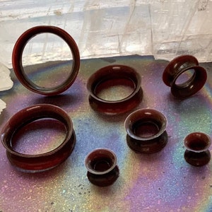 May include: A set of seven brown ear gauges of varying sizes, displayed on a white surface with a rainbow iridescent background.