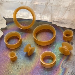 May include: A set of eight brown silicone ear gauges of varying sizes, displayed on a black surface with iridescent rainbow patterns.