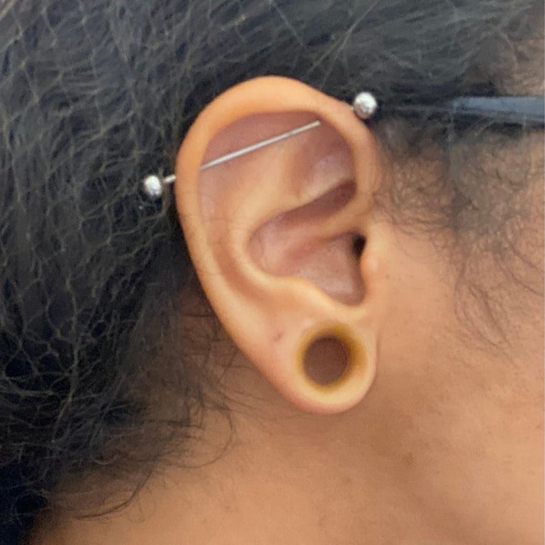 May include: A person with a double helix piercing in their earlobe and a stretched earlobe with a brown plug.