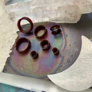 May include: A set of seven brown ear gauges of varying sizes, displayed on a white surface with a rainbow iridescent background.