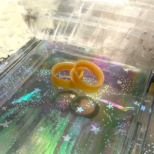 May include: Two beige silicone ear gauges, also known as flesh tunnels, are displayed on a iridescent background with a white crystal in the background.