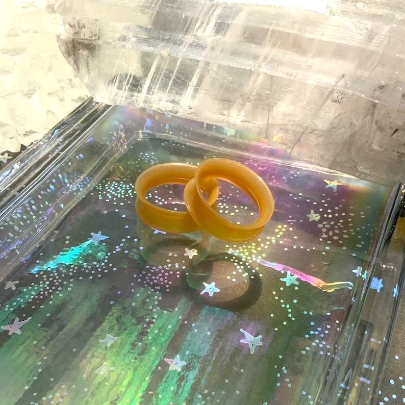 May include: Two beige silicone ear gauges, also known as flesh tunnels, are displayed on a iridescent background with a white crystal in the background.