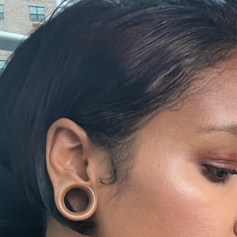 May include: A close-up of a person's ear with a large brown ear gauge. The gauge is a simple circle with a smooth surface.