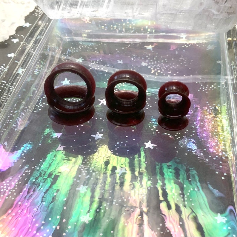 May include: Three dark red silicone ear gauges of different sizes. The gauges are round and have a smooth, polished finish.