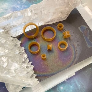 May include: A set of eight brown silicone ear gauges of varying sizes, displayed on a white crystal surface.