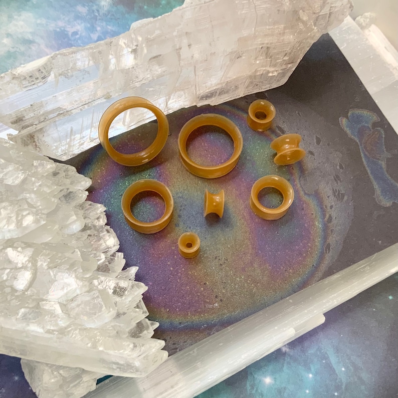 May include: A set of eight brown silicone ear gauges of varying sizes, displayed on a white crystal surface.