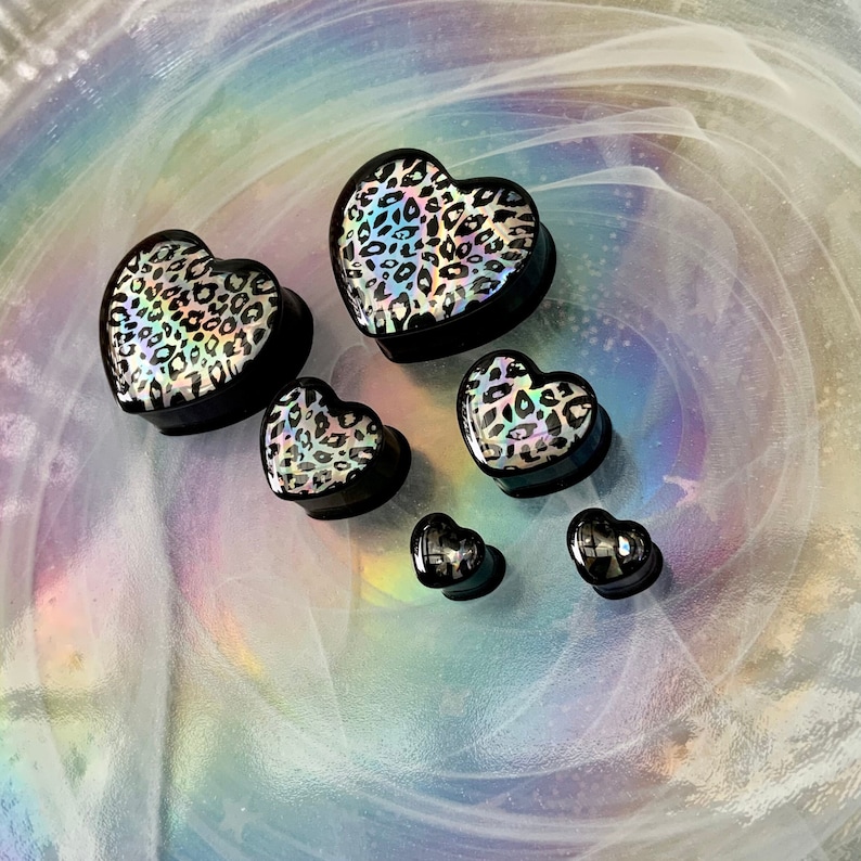 May include: A set of six heart-shaped ear gauges in various sizes. The gauges are black with a leopard print design and iridescent finish.