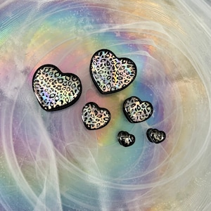 May include: Five black heart-shaped earrings with a leopard print design. The earrings are of varying sizes.