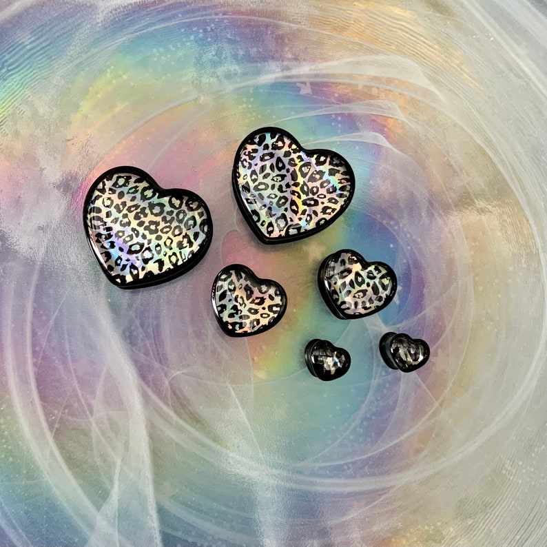 May include: Five black heart-shaped earrings with a leopard print design. The earrings are of varying sizes.