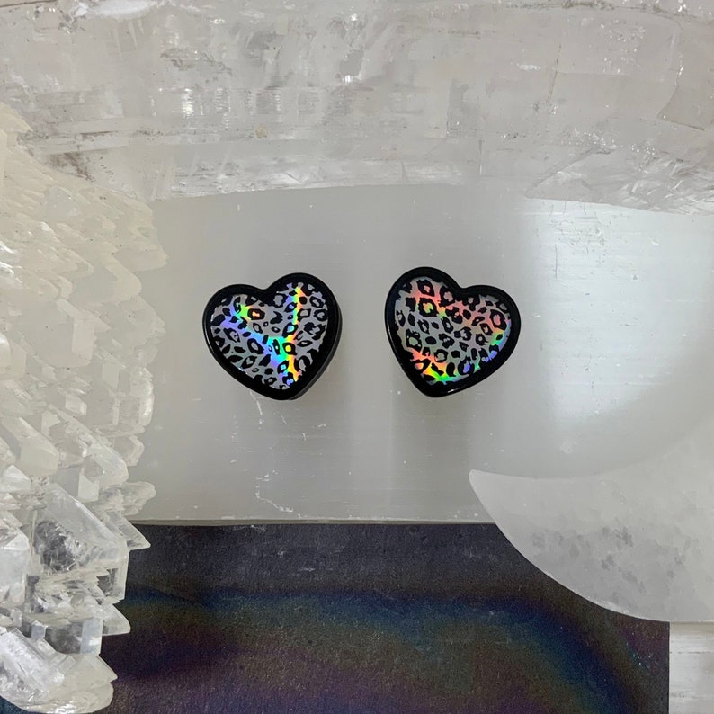 May include: Two black heart-shaped earrings with a holographic leopard print design.