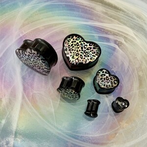 May include: Set of six black heart-shaped ear gauges with a leopard print design. The gauges are made of acrylic and have a shiny finish.
