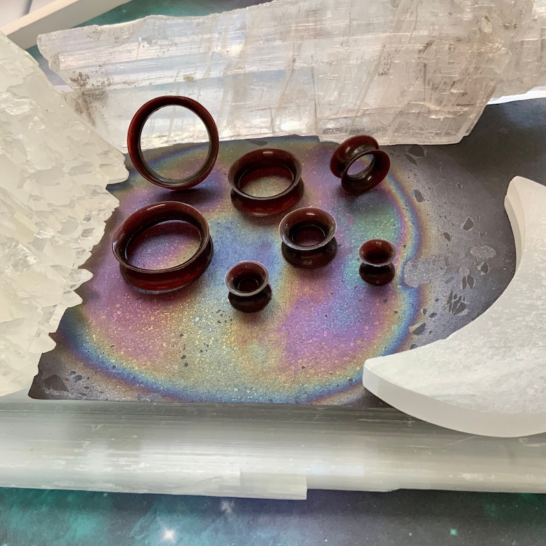 May include: A set of seven brown ear gauges of varying sizes, displayed on a white surface with a rainbow iridescent background.