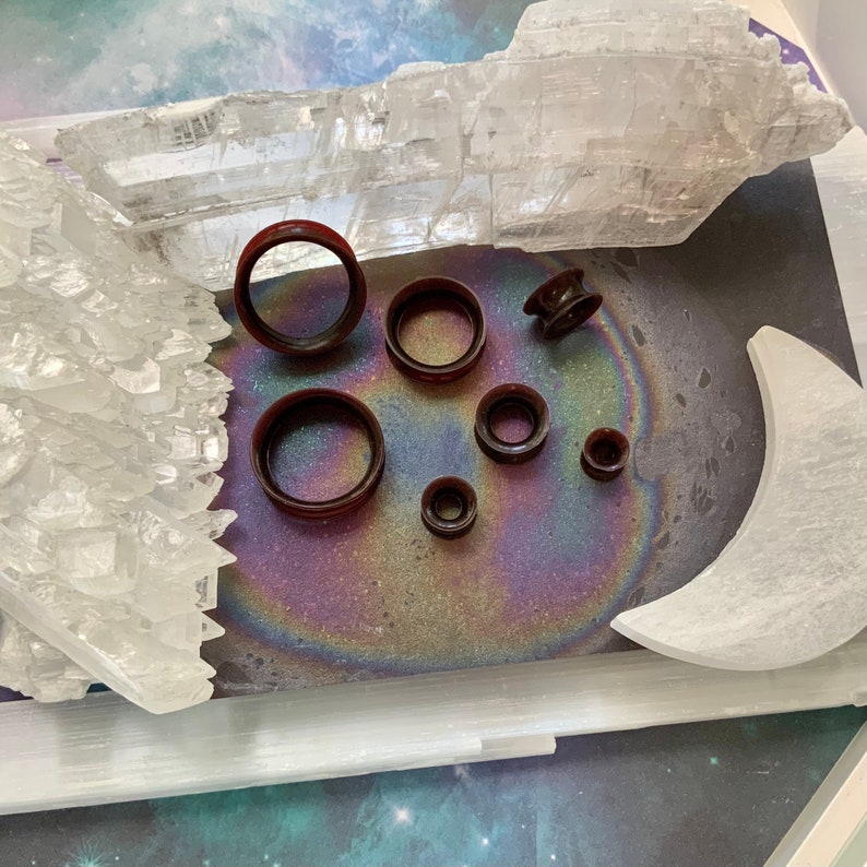 May include: A set of eight brown ear gauges of varying sizes, displayed on a white surface with a rainbow iridescent background.