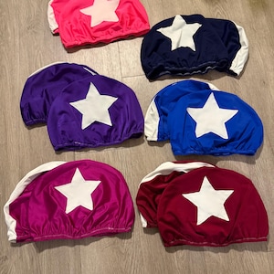 Pode incluir: Uma coleção de bonés de jóquei coloridos em tons de rosa, azul marinho, roxo, azul e bordô. Cada boné apresenta uma grande estrela branca e uma aba branca. Os bonés são feitos de tecido brilhante, ideais para corridas.