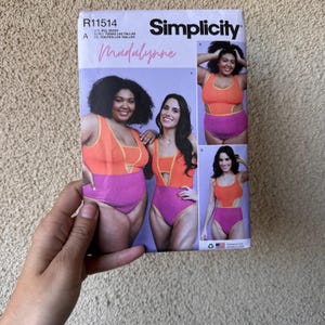 May include: Simplicity sewing pattern R11514 featuring a swimsuit design. The pattern cover shows two women wearing a two-tone swimsuit in orange and purple. The word "Madalynne" is written in cursive.