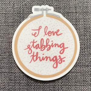 May include: A round sticker with a brown border and a white background. The sticker has a pink and white speckled pattern and the text "I love stabbing things." in pink.