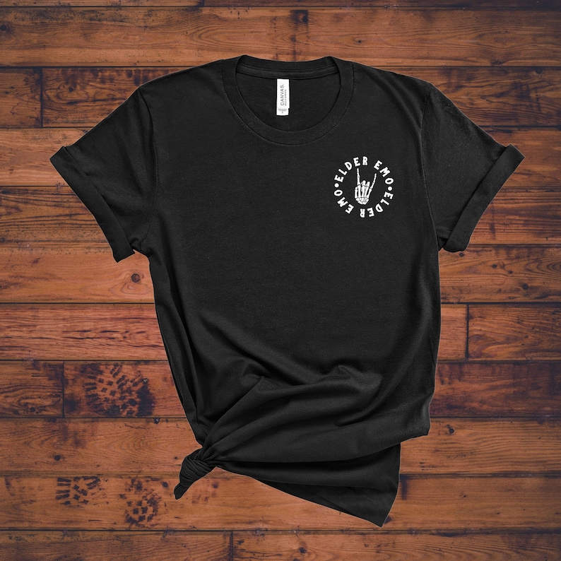May include: Black t-shirt with a white graphic of a skeleton hand making a rock-and-roll gesture, encircled by the words "Elder Emo." The shirt is made of a soft material and has rolled-up sleeves.