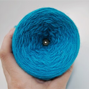 Puede incluir: Un ovillo de hilo azul turquesa con un agujero en el centro.