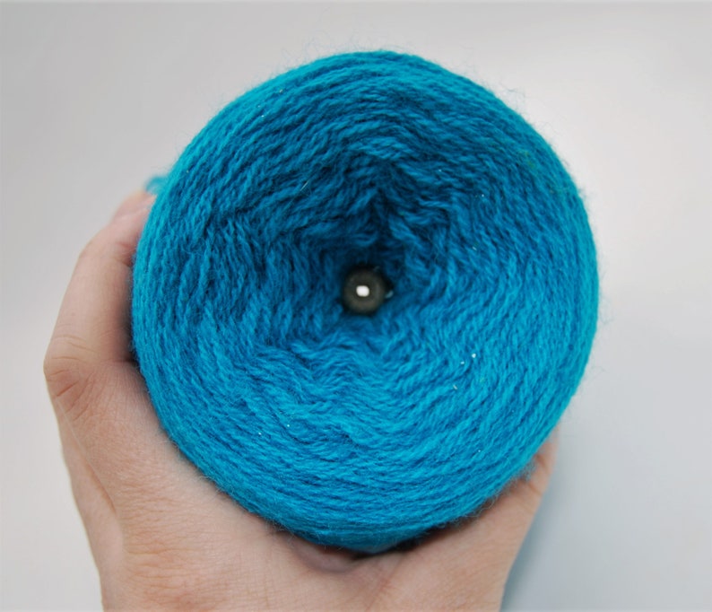 Puede incluir: Un ovillo de hilo azul turquesa con un agujero en el centro.