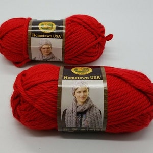 Pode incluir: Dois novelos de fio vermelho com a etiqueta "Hometown USA" da Lion Brand Yarn.