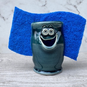 May include: A set of three ceramic mugs with a speckled, cream-colored glaze. Each mug features a different hand-painted design: a blue and green leaf, a yellow and orange flower, and a red berry sprig. The mugs have a simple, rounded shape.